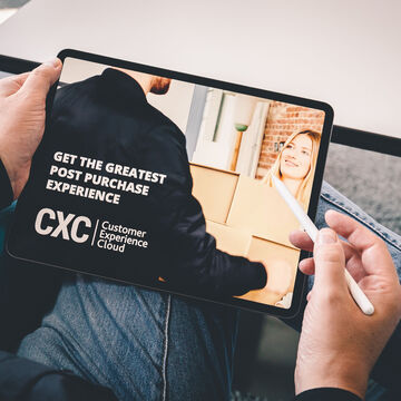 Wir blicken über eine Schulter auf ein Tablet, auf dem die Customer Experience Cloud mit dem Slogan "Get the greatest post purchase experience" beworben wird
