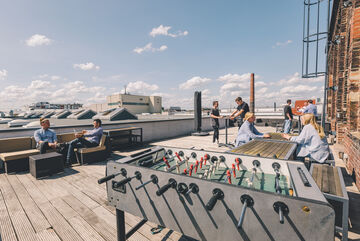 a rooftop terrace under blue skies with a kicker table in the foreground and several employees talking in the background.